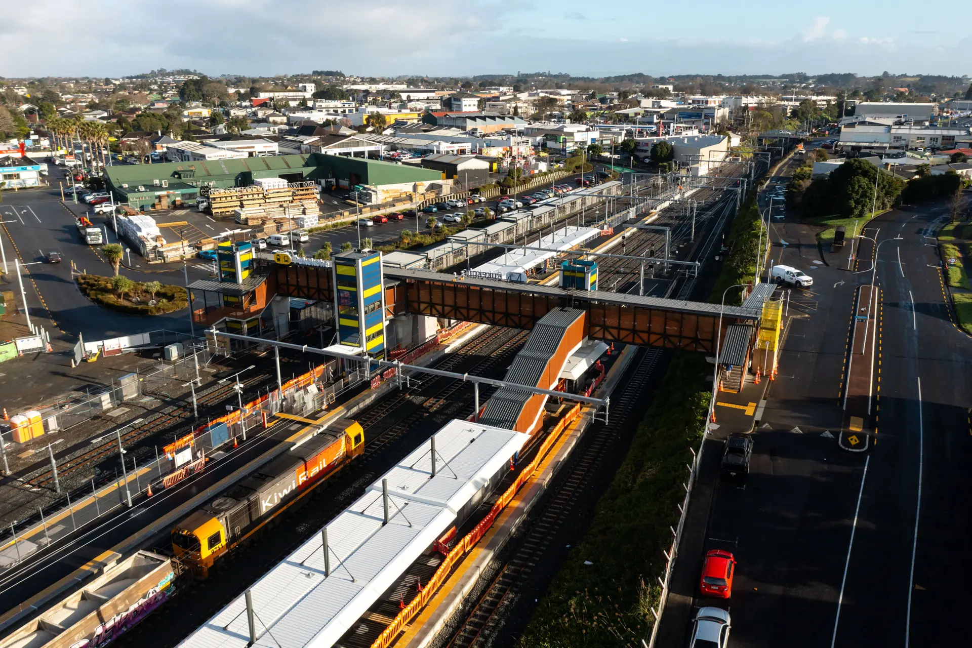 Aerial view of a railway station, with a covered overbridge spanning the tracks and freight and passenger trains at the platforms below.